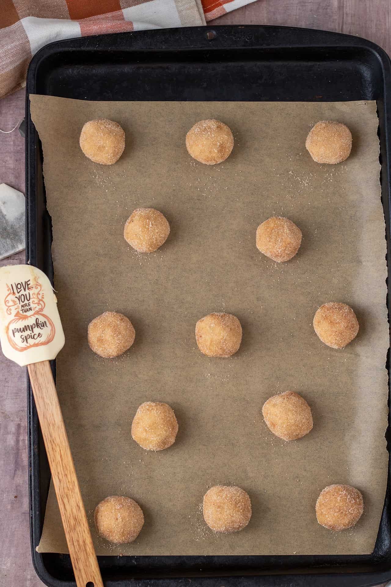 A cookie sheet lined with brown parchment paper topped with balls of snickerdoodle cookie dough.