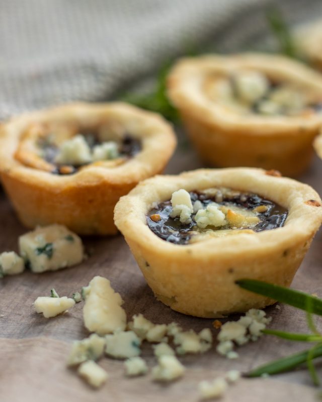 3 mini rosemary shortbread tarts with fresh rosemary sprig and gorgonzola cheese crumbles in the background.