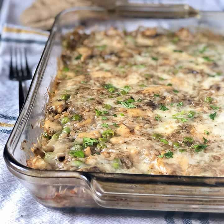 A cheesy and creamy low carb casserole dish made with cauliflower rice, brie cheese, mushrooms and peas. A glass of white wine and an oven mitt are placed in the background