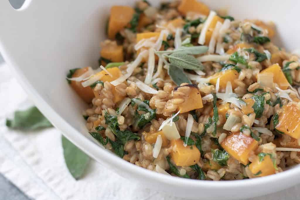 A serving bowl filled with farro risotto with cubes of butternut squash and topped with freshly grated Parmesan cheese and fresh sage leaves