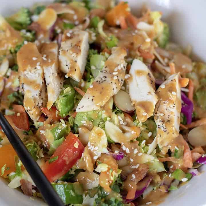 A white bowl filled with crunchy Asian salad with red peppers, cabbage, almonds, broccoli and lettuce. It’s drizzled with a delicious orange sesame peanut dressing and topped with slivered almonds and sesame seeds. It’s easy, healthy and low carb.