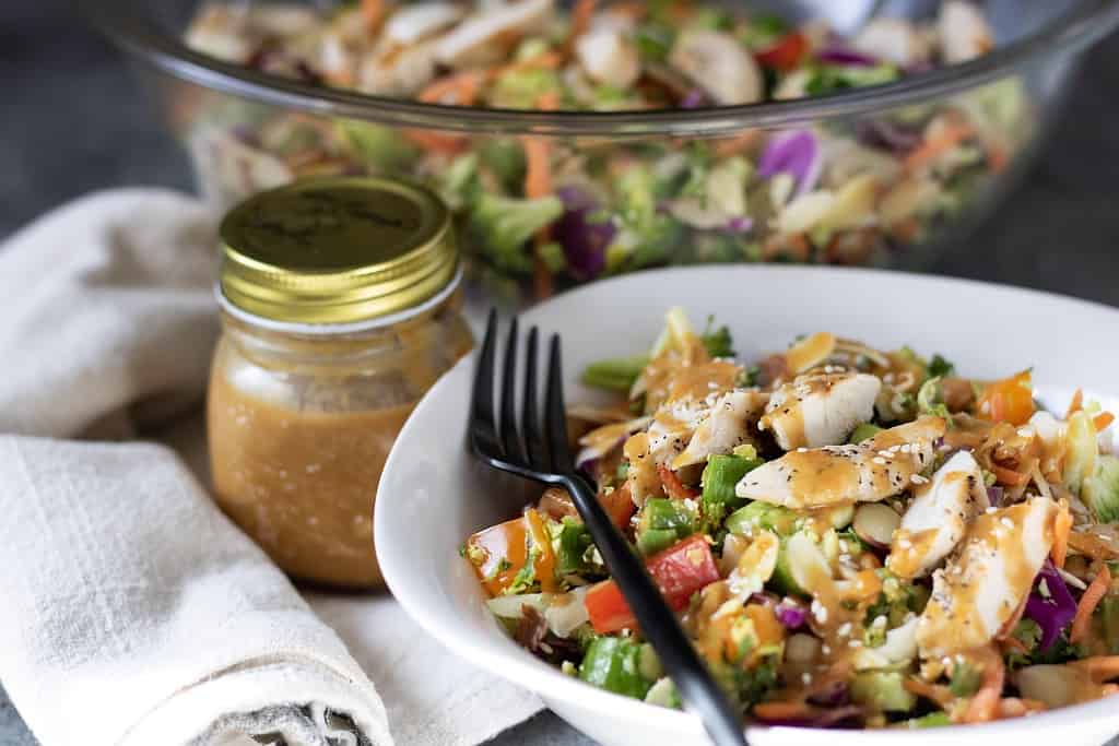 Chopped Asian salad with sesame peanut dressing and grilled chicken. A jar of Asian dressing is next to the bowl with a big bowl of salad in the background.
