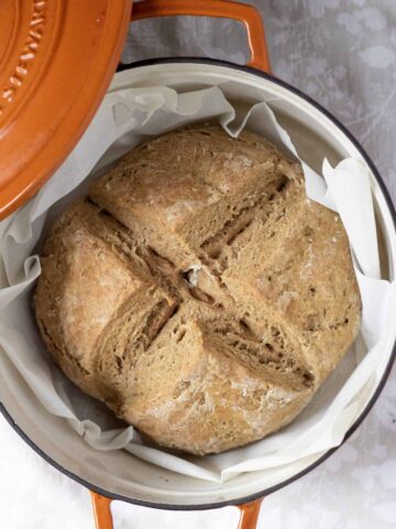 An overhead shot of a baked traditional Irish soda bread in an orange Dutch oven pan.