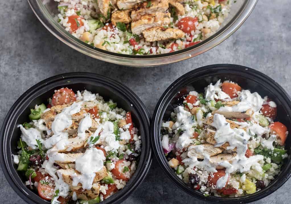 Containers filled with cauliflower Rice, Greek chicken, olives, tomatoes, cucumbers and chickpeas. They’re perfectly packed for an easy meal prep for lunch on the go.