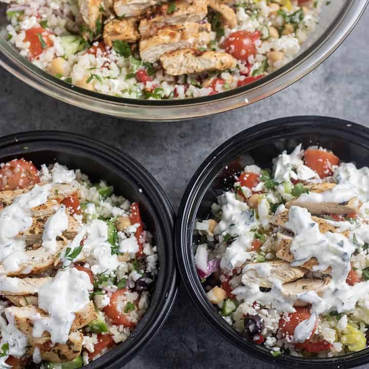 Containers filled with cauliflower Rice, Greek chicken, olives, tomatoes, cucumbers and chickpeas. They’re perfectly packed for an easy meal prep for lunch on the go.