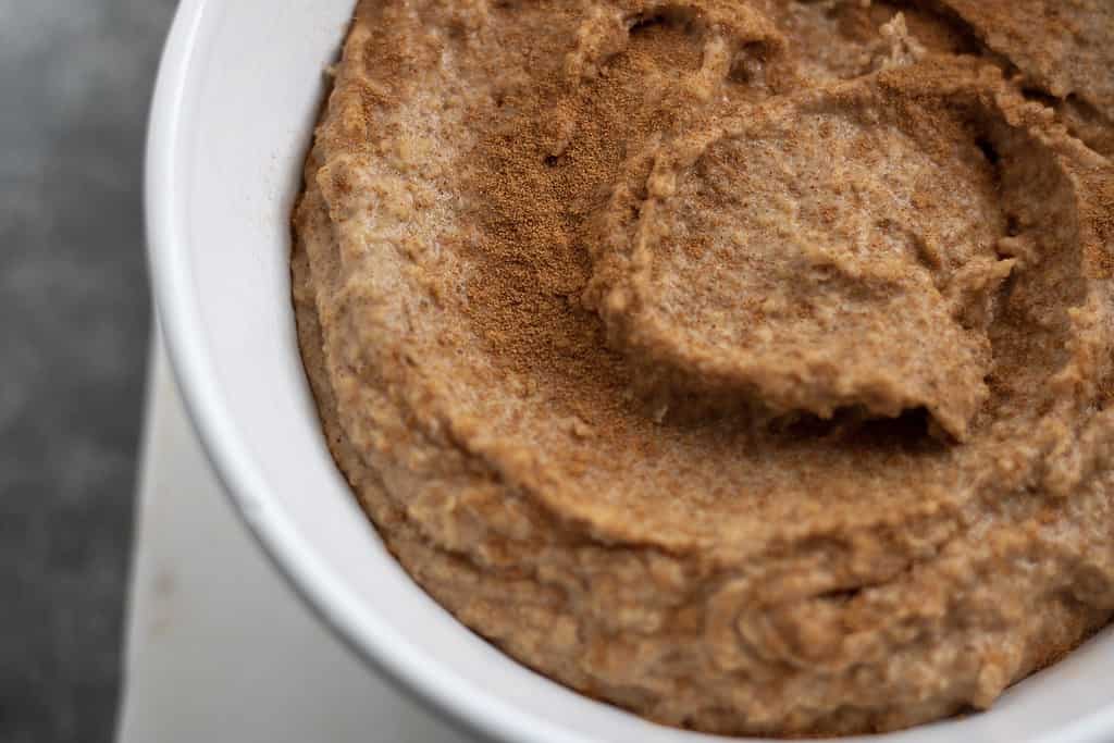 A closeup picture of Snickerdoodle Hummus in a white bowl. Sprinkled with cinnamon, it’s and easy and healthy snack recipe. Made without tahini and in less than 5 minutes!