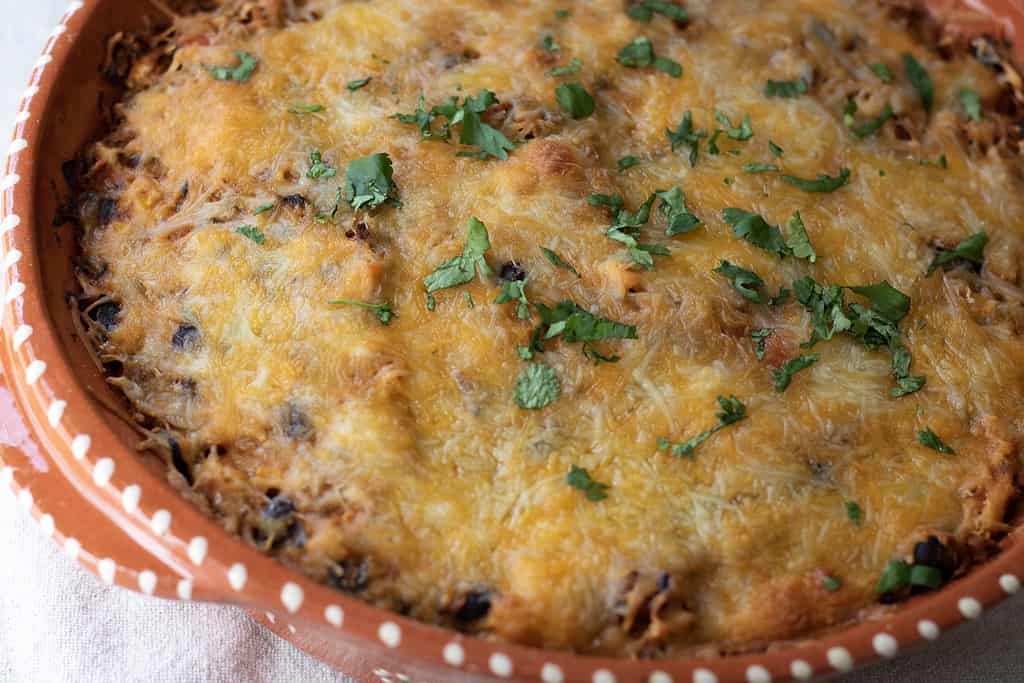 A round casserole dish with Mexican casserole that’s topped with cheese and cilantro. It’s made with shredded chicken, cauliflower rice, black beans, corn and red peppers for an easy and healthy recipe.