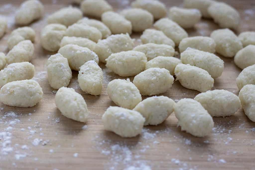Homemade cauliflower gnocchi that’s been shaped by hand on a wooden cutting board dusted with flour