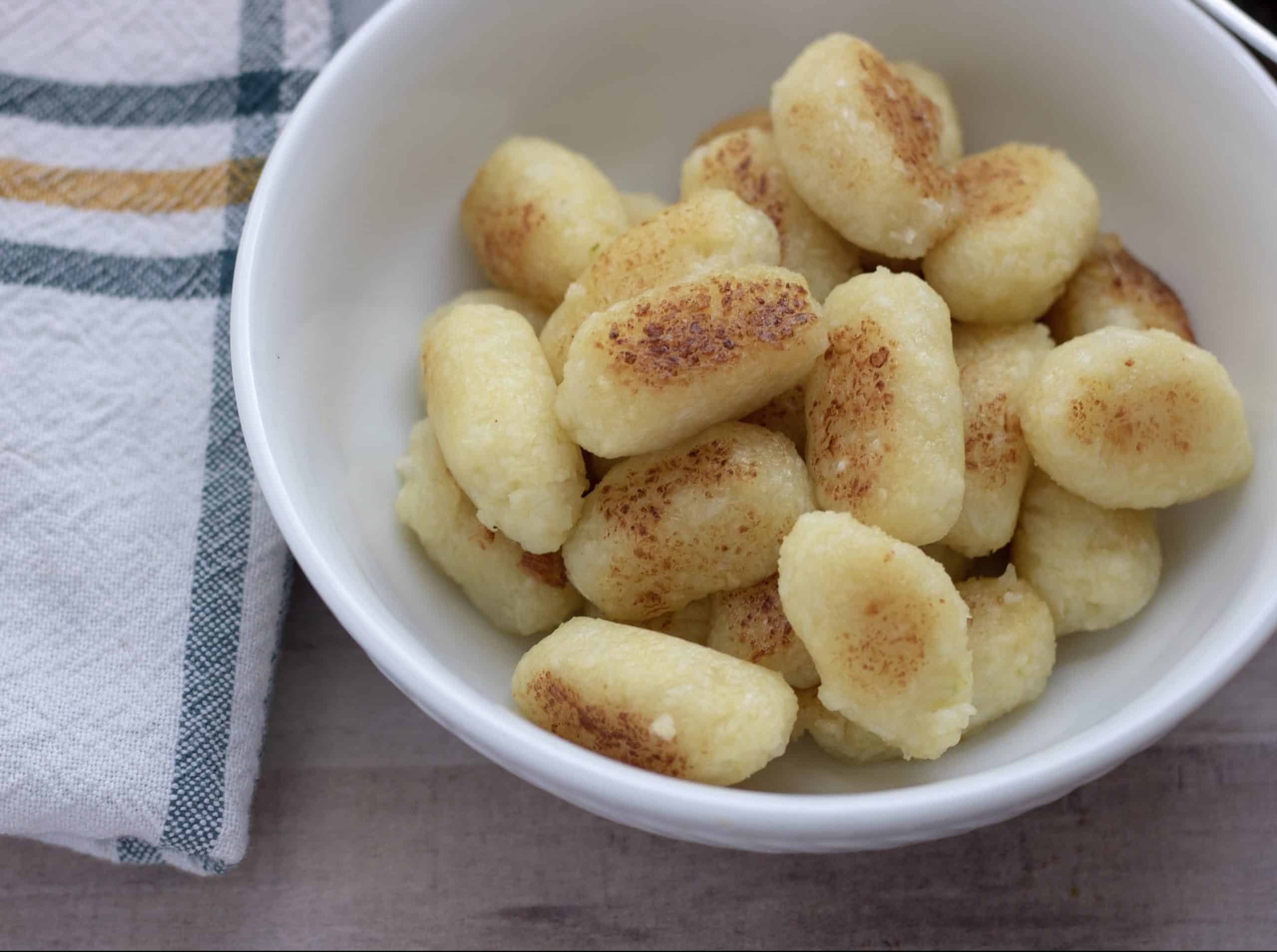 A white bowl of homemade cauliflower gnocchi that have been pan fried and golden. They’re a copy cat version of Trader Joe’s