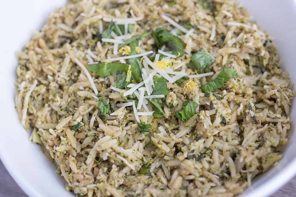 A white bowl full of orzo pasta with broccoli rice, lemon and balsamic. Fresh basil, Parmesan and lemon zest are sprinkled on the top
