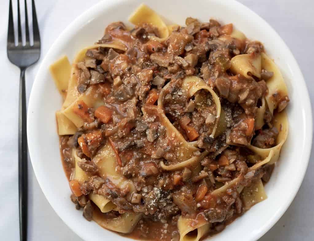 An overhead shot of Italian bolognese made from mushrooms, eggplant and carrots. It’s served with fresh grated Parmesan cheese over pappardelle pasta