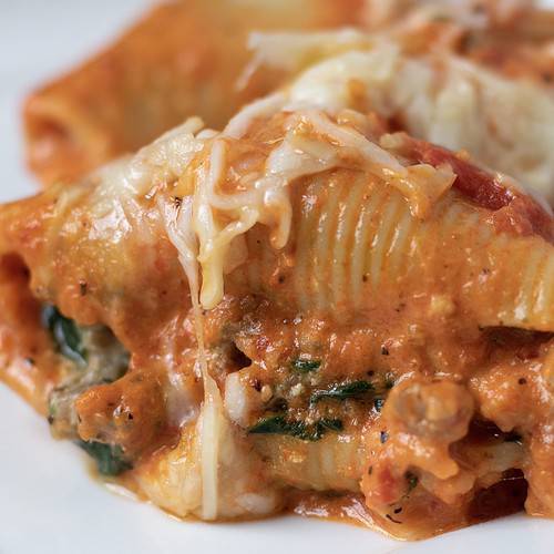 A white square dish with 3 stuffed shells that are covered in a creamy red peppers sauce and melted mozzarella cheese.