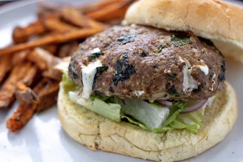 Spinach and mozzarella stuffed turkey burgers. The burger is on a bulkie roll with lettuce and onion and a side of sweet potato fries