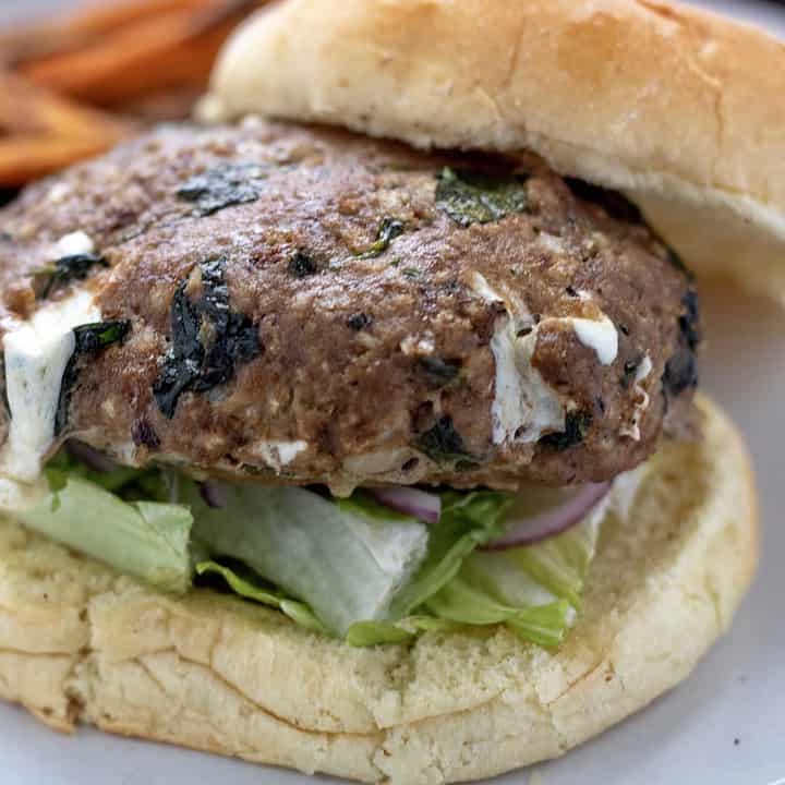 Spinach and mozzarella stuffed turkey burgers. The burger is on a bulkie roll with lettuce and onion and a side of sweet potato fries