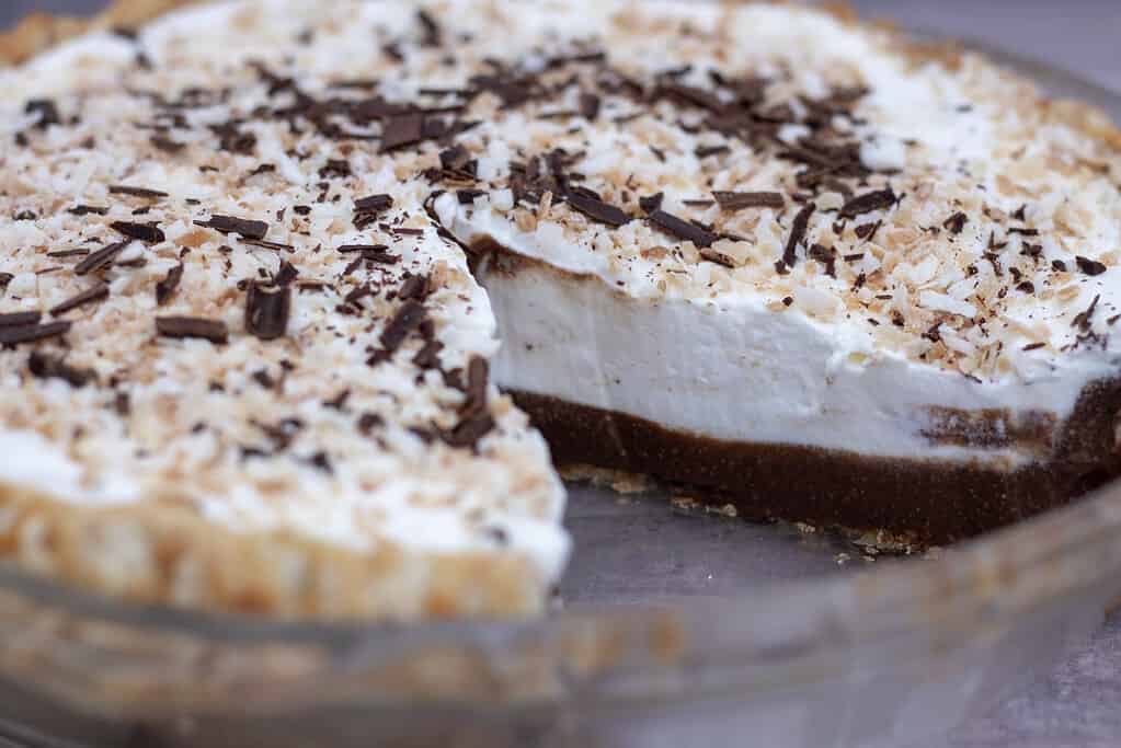 A whole chocolate coconut cream pie with a slice taken out. You can see the creamy homemade chocolate filling inside that’s topped with whipped cream and toasted coconut