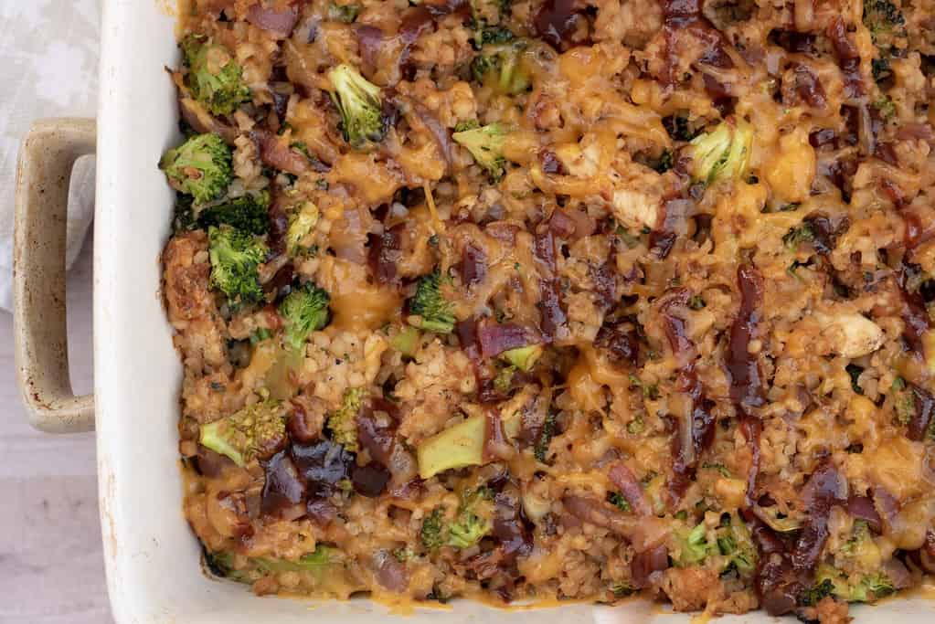 A cheesy low carb casserole made with cauliflower rice, broccoli, bbq chicken and cheese. The BBQ sauce is drizzled on top and the cheesy is melted and golden