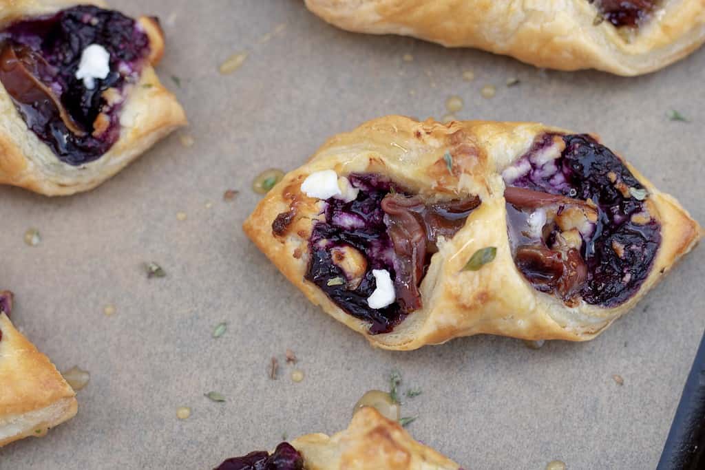 Puff pastry appetizers are filled with savory blueberry, Goat cheese and prosciutto and the edges are folded together. They’re baked until golden brown and drizzled with a thyme infused honey