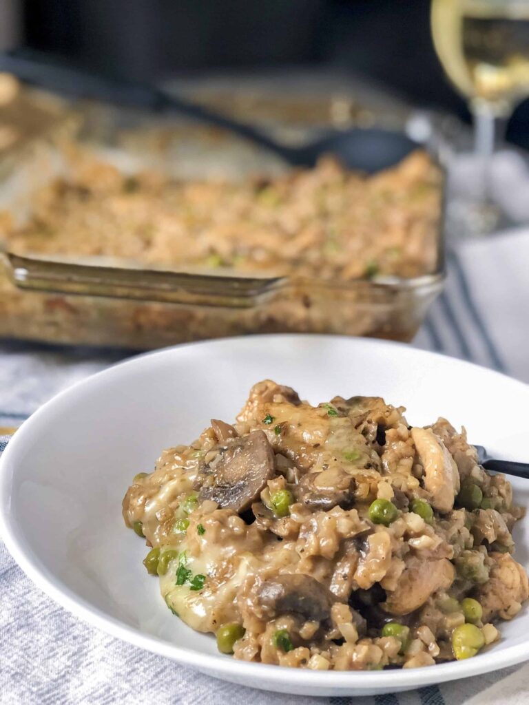 A cheesy and creamy low carb casserole dish made with cauliflower rice, brie cheese, mushrooms and peas. A glass of white wine and an oven mitt are placed in the background