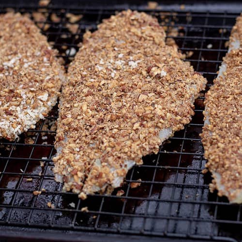 3 Pieces of white fish crusted with toasted pecans and placed on a baking sheet to be baked in the oven.
