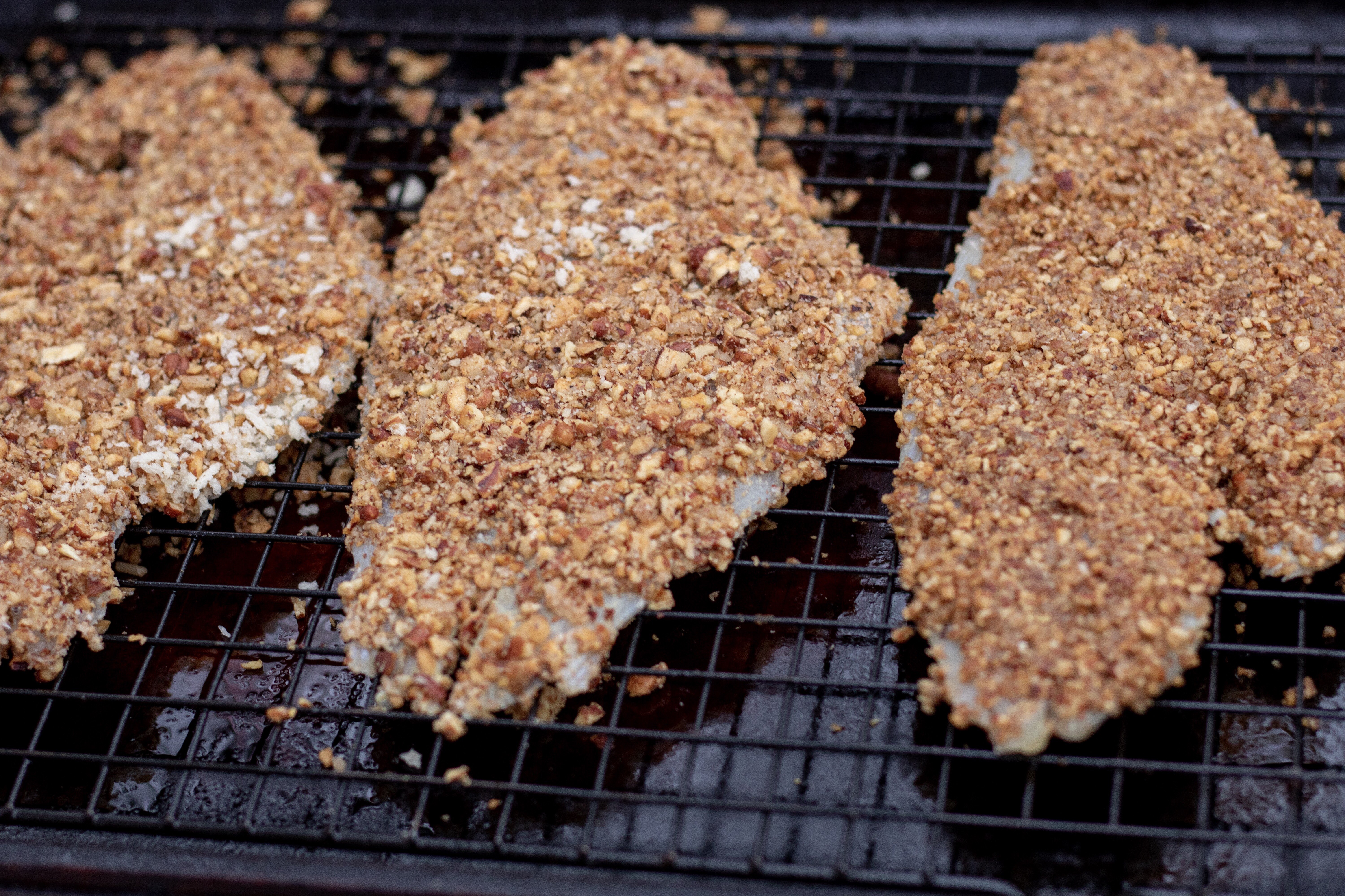 3 Pieces of white fish crusted with toasted pecans and placed on a baking sheet to be baked in the oven.