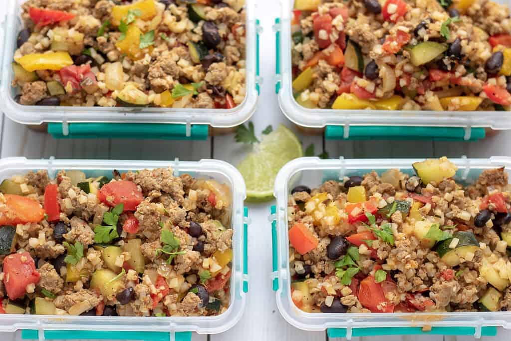 Four small containers filled with mexican cauliflower rice that's made with black beans, peppers, tomatoes and zucchini. It's an easy and low carb meal prep recipe for lunch or dinner on the go.