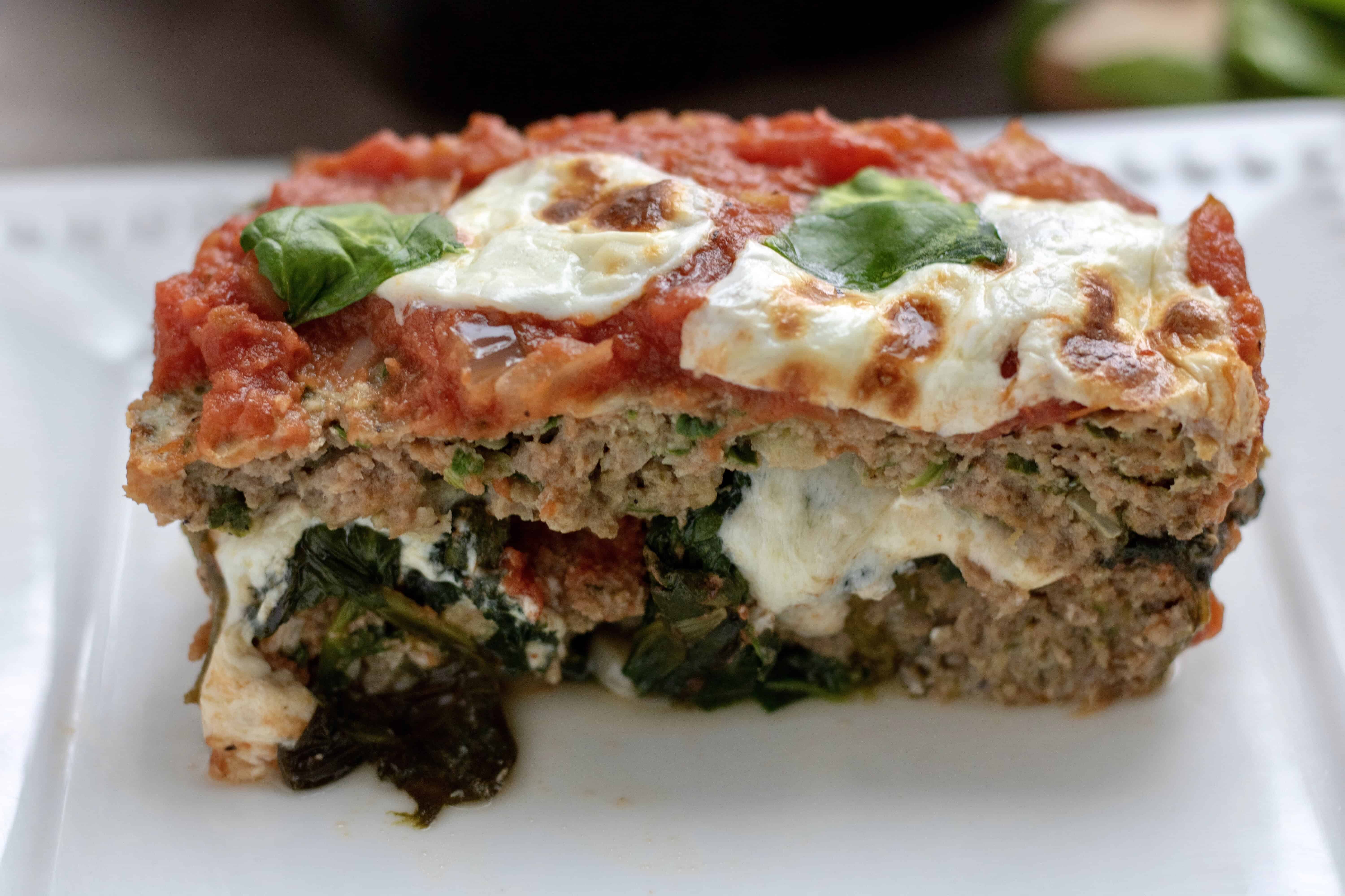 A white rectangle dish with a big slice of meatloaf. It’s made with ground chicken, fresh spinach and fresh mozzarella. It’s topped with marinara sauce for an easy Italian meatloaf recipe perfect for a healthy family dinner