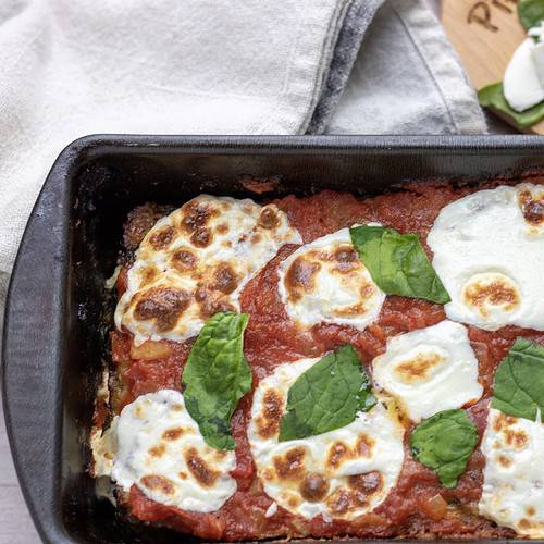 A loaf pan of Italian meatloaf that’s topped with marinara and fresh mozzarella slices that are melted and slightly golden. It’s finished with fresh basil slices.