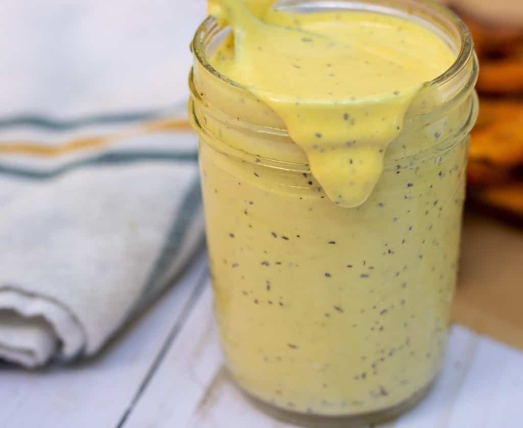 A small mason jar filled with maple mayo sauce. It's overflowing down the sides of the jar. It's thick and creamy with specks of black pepper.