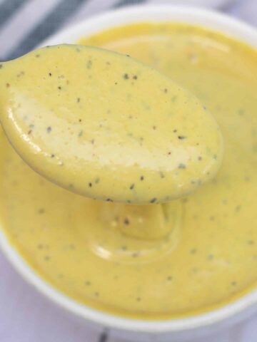A small white bowl of maple mayo mustard sauce with a spoonful of sauce dripping into the bowl.