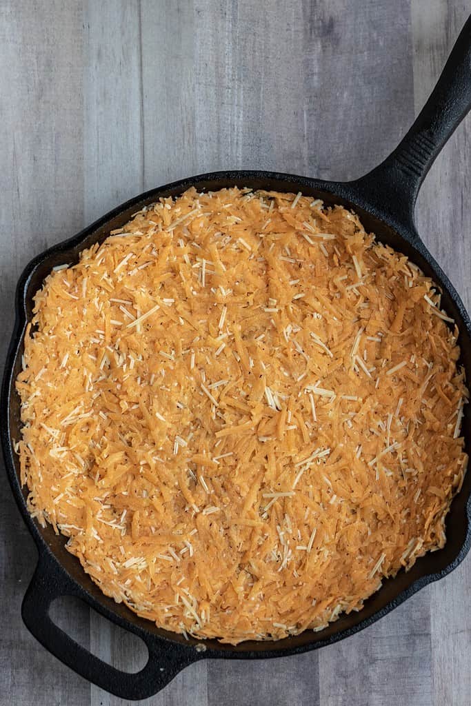 A cast iron skillet with a shredded sweet potato Parmesan crust for quiche