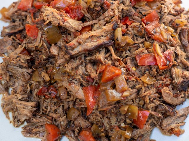 a while bowl full of tender shredded crockpot chipotle barbacoa taco meat. It’s got chopped red bell peppers and onions mixed it. It’s slightly browned and very tender.