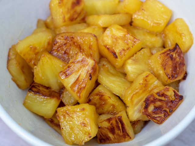 A white bowl of pineapple chunks that have been caramelized with brown sugar until golden.