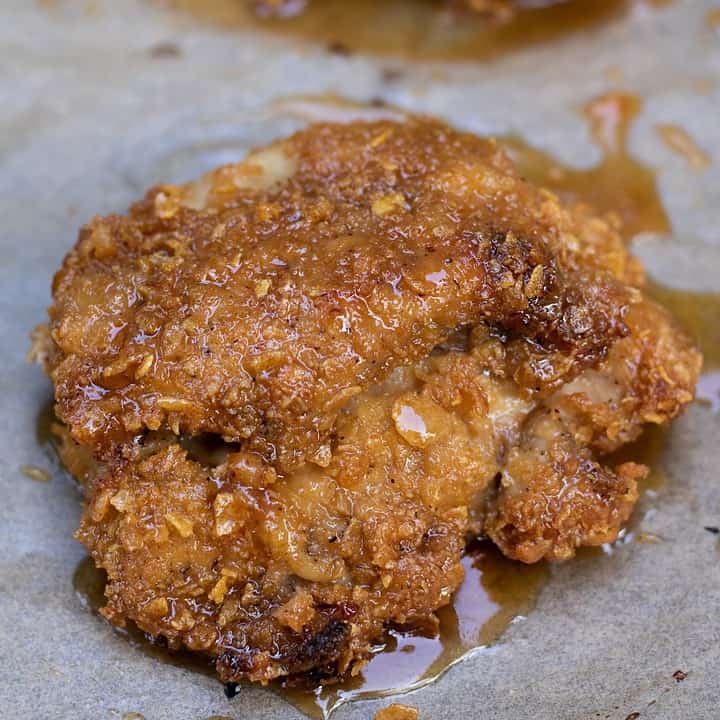Golden and crispy baked chicken thighs that are drenched in a hot honey sauce. The honey is dripping down onto the brown parchment paper lined baking sheet.