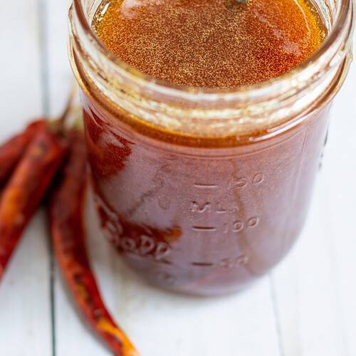 A mason jar filled with honey with dried red chili peppers in the background.