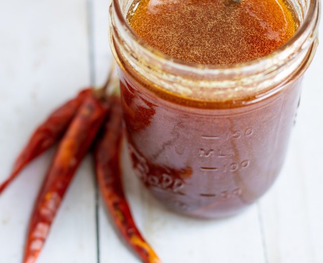 A mason jar filled with honey with dried red chili peppers in the background.
