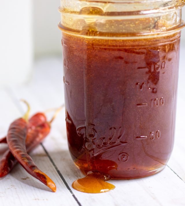 A mason jar filled with honey that's over flowing down the side. A couple of red dried chiles are next to the mason jar.