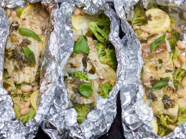 3 foil packets filled with white fish and vegetables like broccoli and yellow summer squash. It’s topped with fresh basil and a lemon garlic butter sauce.