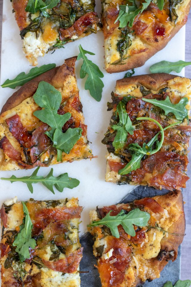 Cut up pieces of flatbread naan pizza that’s topped with crispy salami pieces, fresh arugula and cheeses. The salami is browned and crispy on top.