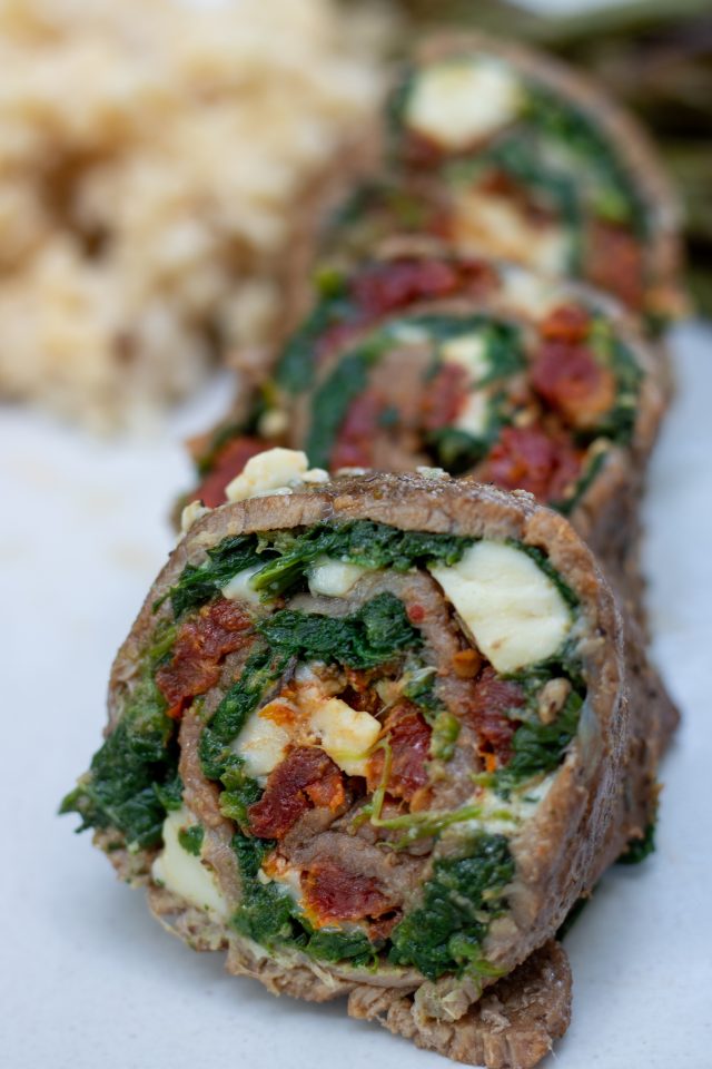 sliced steak roll ups that look like pinwheels. You can see they’ve been stuffed with cheese, spinach and sun dried tomatoes. There’s 3 round slices on a serving plate.