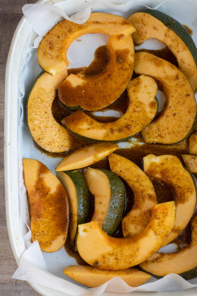 A large white rectangle baking dish lined with parchment paper. There's slices of acorn squash that have a maple curry glaze on them.