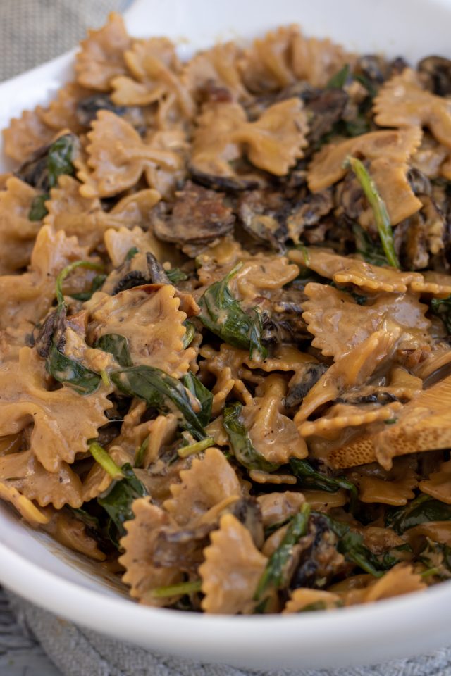 A large white bowl filled with farfalle pasta with spinach and mushrooms.  It's tossed in a balsamic cream sauce.