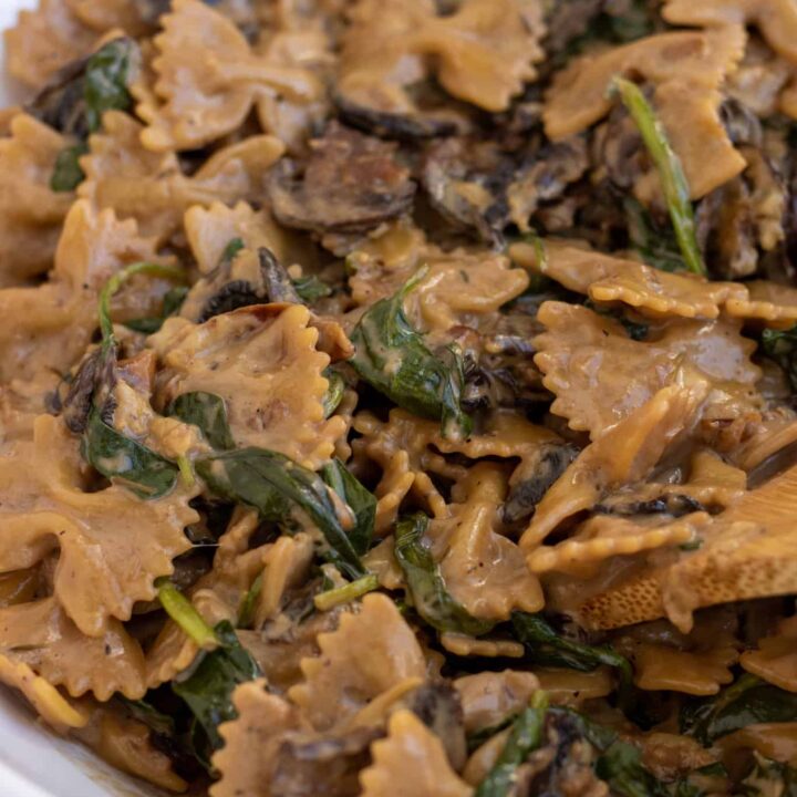 A large white bowl filled with farfalle pasta with spinach and mushrooms. It's tossed in a balsamic cream sauce.