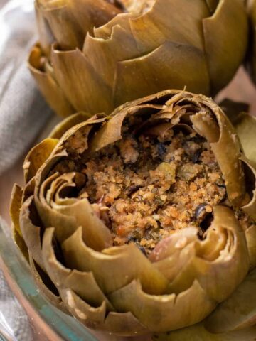 A glass baking dish filled with italian stuffed artichokes. They've been steamed and the leaves are opened up like flowers. They're stuffed with a breadcrumb stuffing.