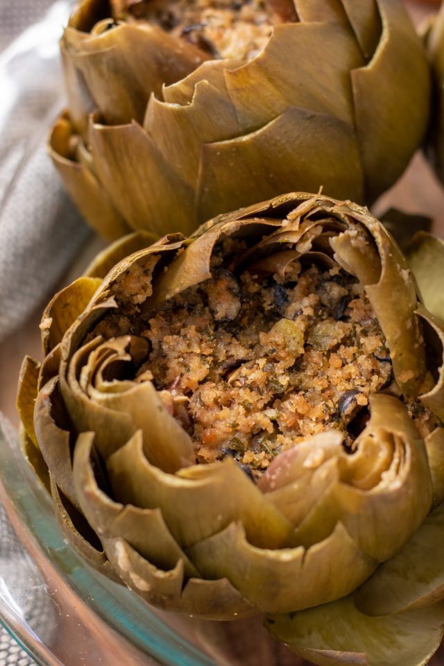 A glass baking dish filled with italian stuffed artichokes. They've been steamed and the leaves are opened up like flowers. They're stuffed with a breadcrumb stuffing.
