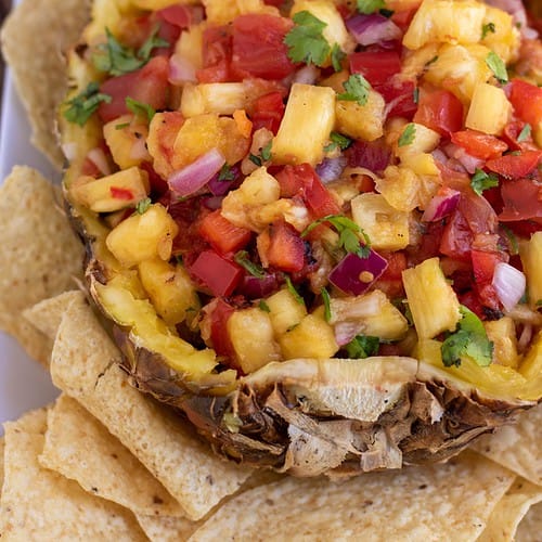 A half of a pineapple filled with fresh salsa and sprinkled with fresh cilantro. There’s tortilla chips around the salsa and it’s bright and vibrant