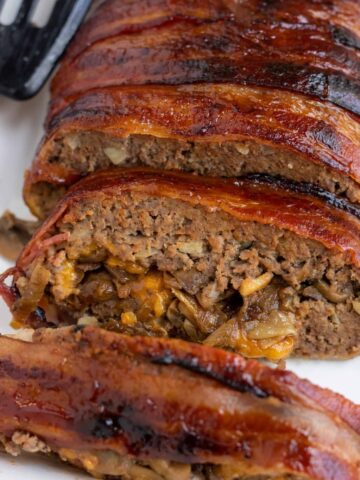 A loaf of meatloaf wrapped in bacon and stuffed with mushrooms, onions and cheddar cheese.