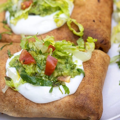 Three chimichangas that are topped with sour cream, shredded lettuce and guacamole. They're dark brown and crispy from the air fryer.