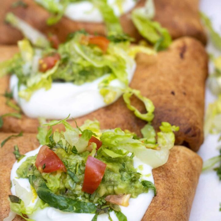 Three chimichangas that are topped with sour cream, shredded lettuce and guacamole. They're dark brown and crispy from the air fryer.