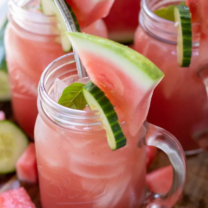 mason jar drink glasses filled with watermelon lemonade. They're garnished with a cucumber slice and small lemon wedge on the rim.