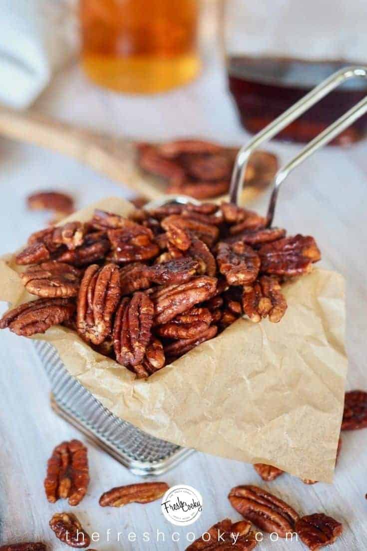 Candied pecans with bourbon and maple on brown parchment paper.  There's a wooden spoon in the background.